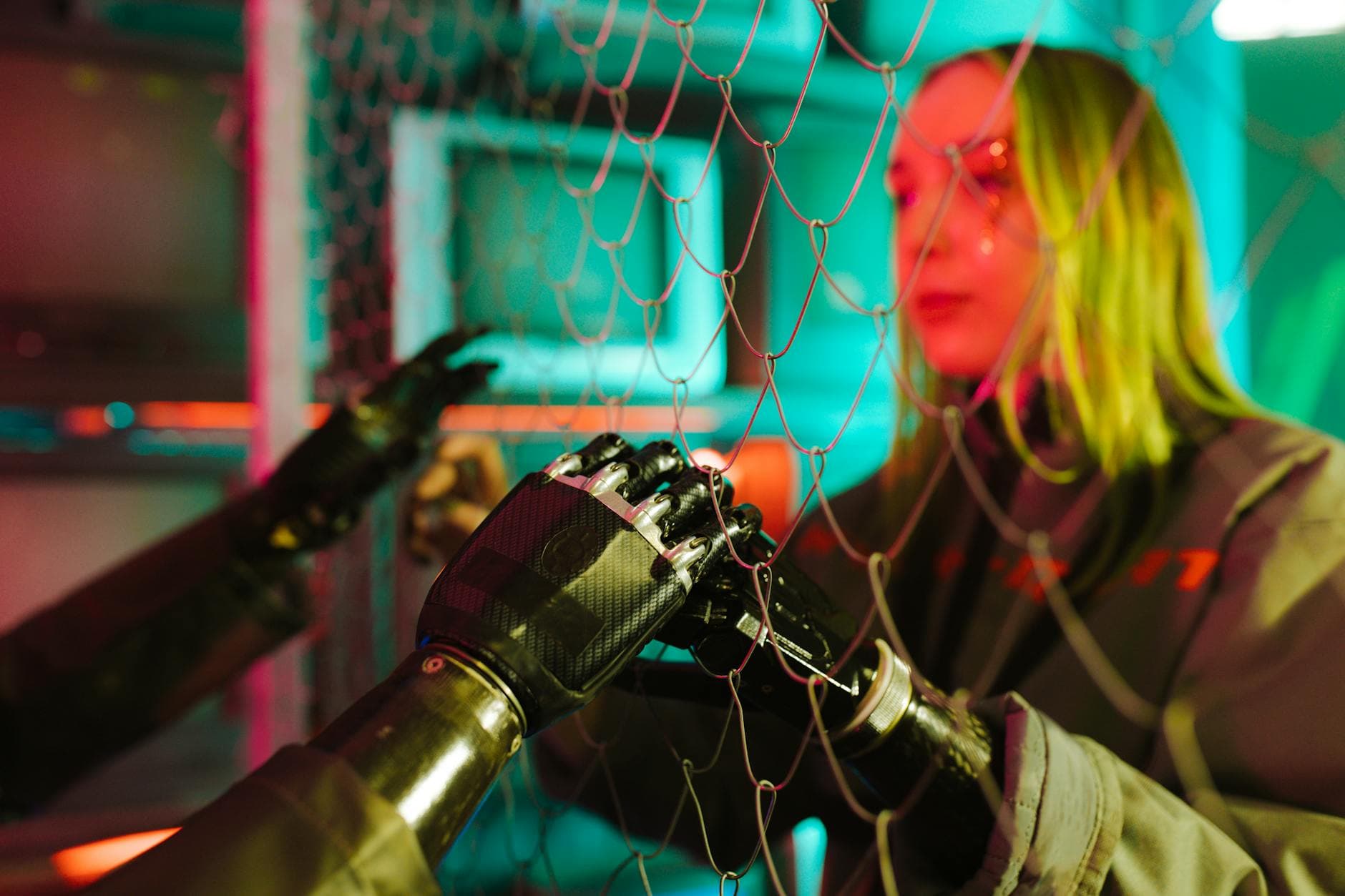 A woman interacts with robotic hands through a mesh displaying a neon cyberpunk atmosphere.