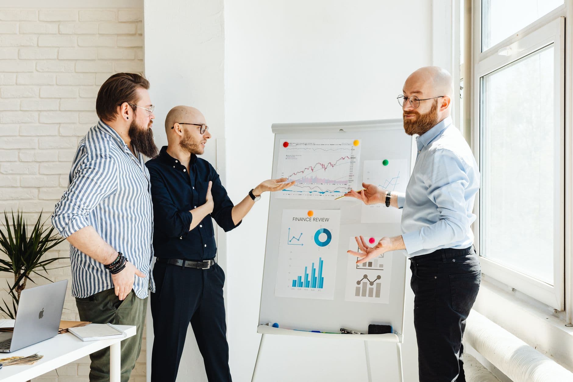 Three colleagues discussing financial charts during a business meeting in a modern office setting.